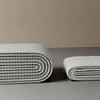 A stack of white no-drill magnetic shower curtains with a waffle texture on a gray surface.