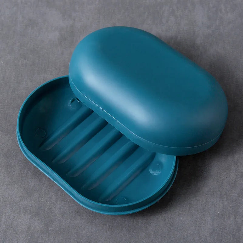 A teal portable soap holder with a lid is shown resting on a gray surface.