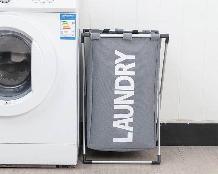 A gray foldable waterproof laundry basket hanging on a metal rack next to a white washing machine.