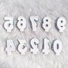 A collection of white candles shaped like letters and numbers resting on a fluffy white surface.