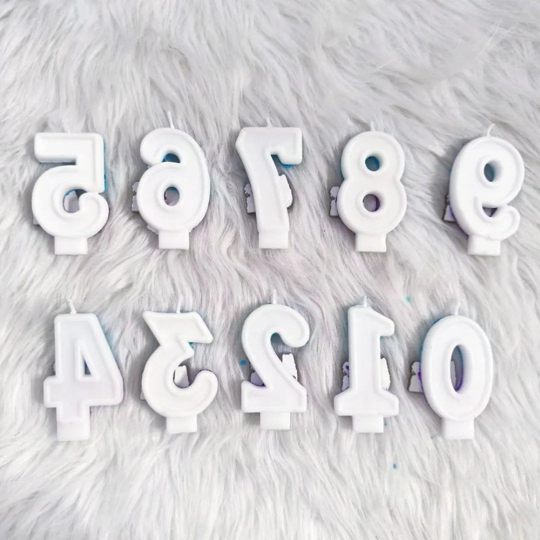 A collection of white candles shaped like letters and numbers resting on a fluffy white surface.