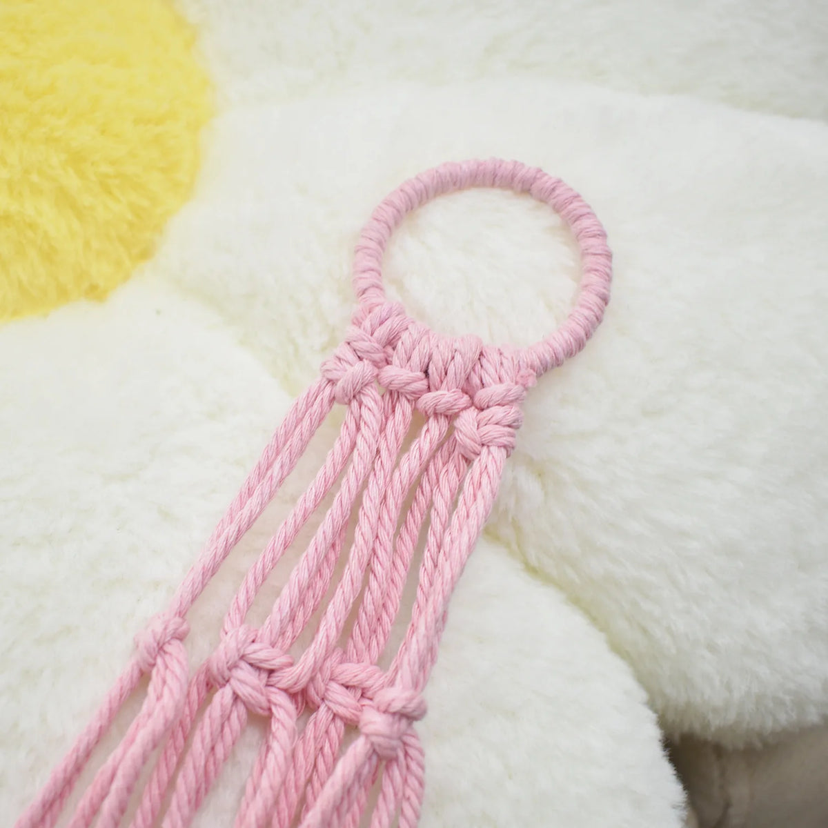 Pink crocheted hammock for a stuffed animal resting on a white fluffy surface.