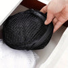 A hand is holding a black collapsible mesh laundry basket with side pockets inside a white box.
