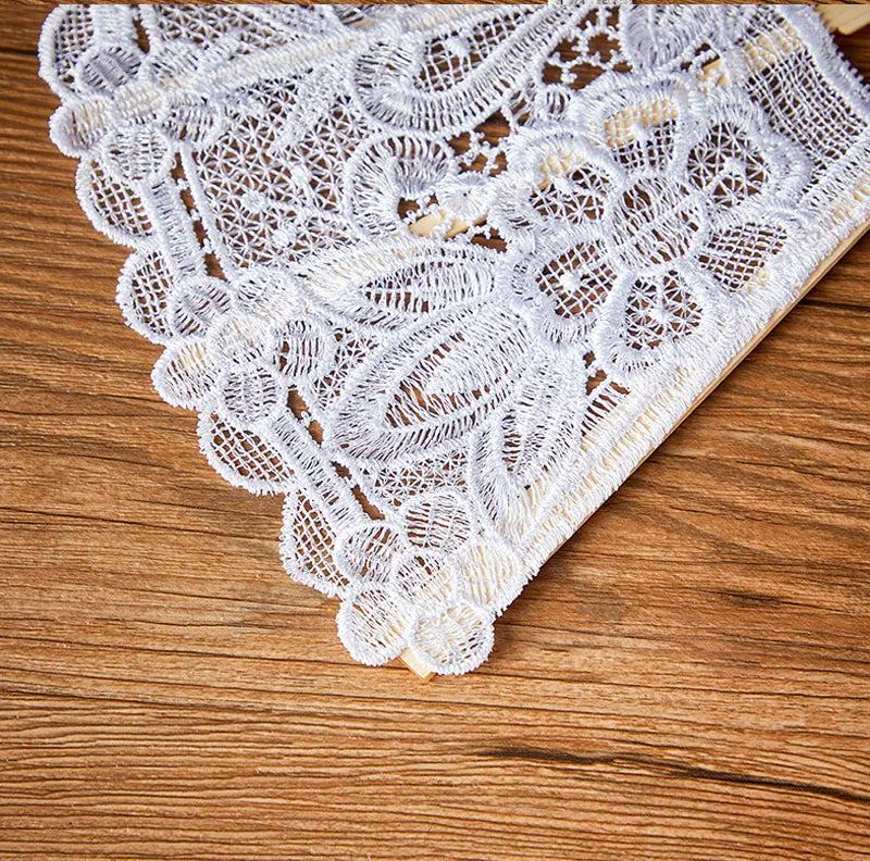 White delicate lace folding handheld fan resting on a wooden surface.