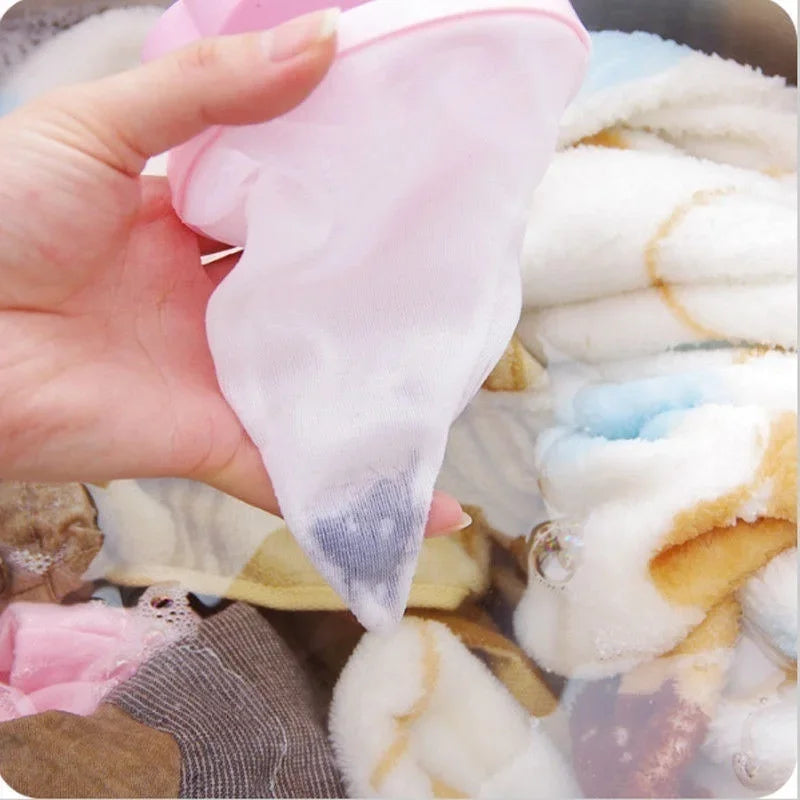 A hand is holding a pink floating laundry mesh filter bag filled with white lint and hair.