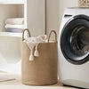 A large woven storage hamper with handles sits next to a white washing machine and stacked towels.