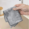 A hand is holding a textured, gray non-stick wire cleaning dish rag over a white sink.