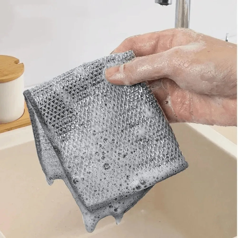 A hand is holding a textured, gray non-stick wire cleaning dish rag over a white sink.