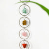 A series of five polished crystal pendants suspended on a silver chain, featuring green, yellow, pink, and red stones.