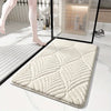 A rectangular beige plush non-slip bathroom rug is shown on a white marble floor next to a glass panel.