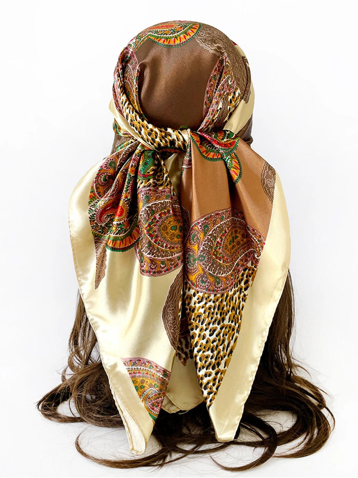 A square paisley print scarf in gold and brown tones tied around a dark hair