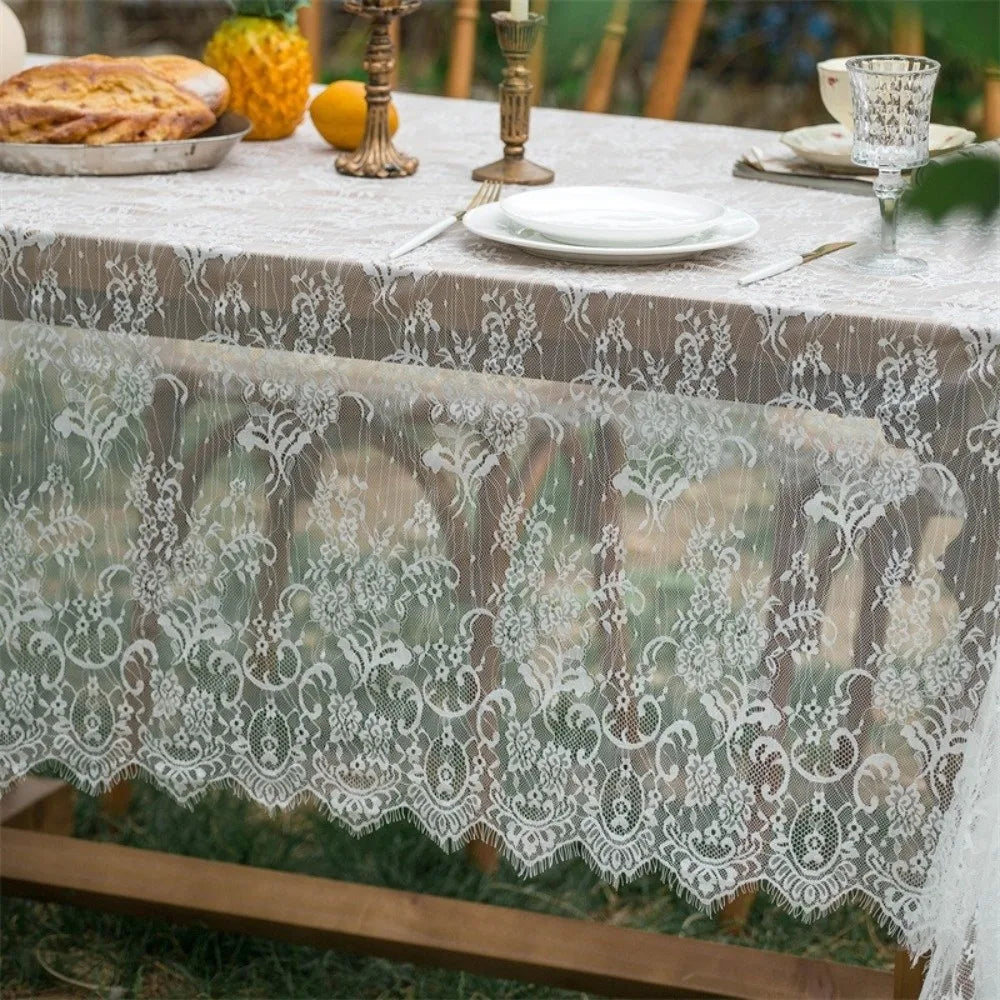 A table set with a lace retro tablecloth and decorative elements outdoors.