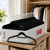 A set of black velvet hangers with chrome hooks is displayed on a wooden shelf.