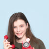 A young woman holds a red retro phone money jar prop against a light blue background.