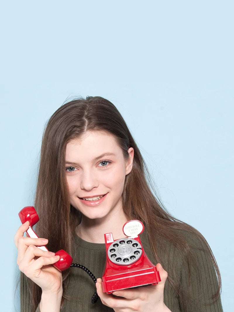 A young woman holds a red retro phone money jar prop against a light blue background.