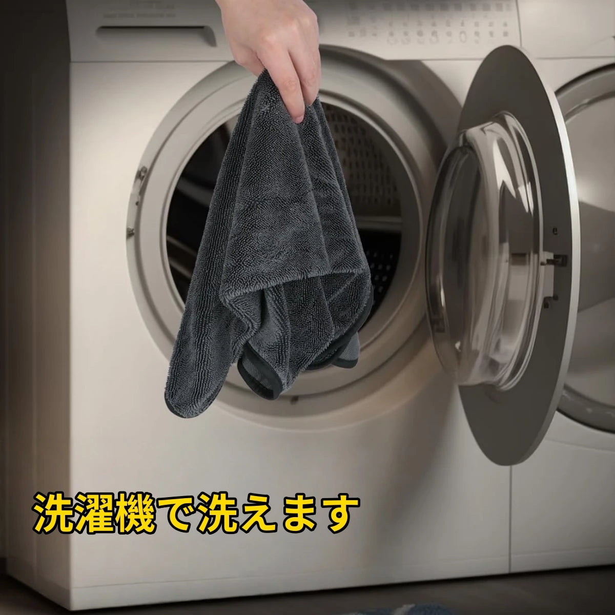 A hand is placing a gray microfiber drying towel into the drum of a washing machine.