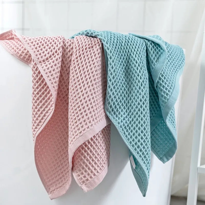 Ein Set aus rosa und hellblauen Waffel-Strangbadhandtüchern, die an einem weißen Haken hängen.