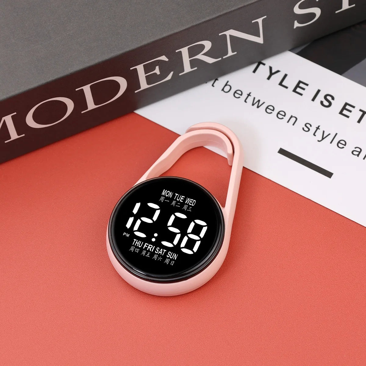 A pink digital LED hanging pocket watch displaying 12:58 on a red surface.