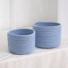 A light blue handwoven cotton rope storage basket sitting on a white surface.