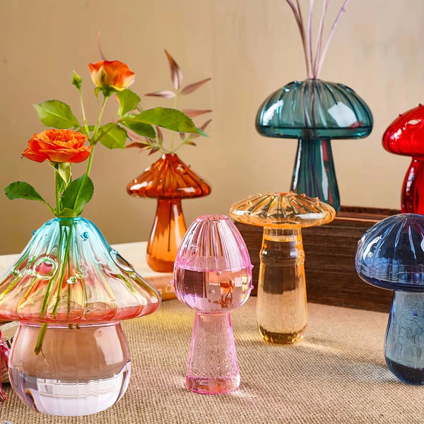 A collection of glass mushroom-shaped vases in various colors like pink, orange, and blue resting on a table.