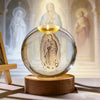 A clear glass crystal ball featuring an engraved image of the Virgin Mary, set on a wooden base.
