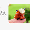 A small, orange resin figurine of a Highland cow with white horns and black details resting on a person's finger.