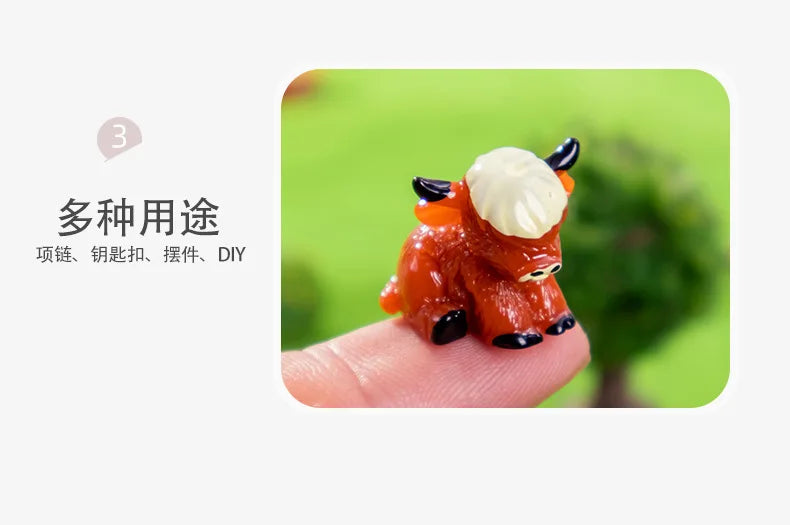 A small, orange resin figurine of a Highland cow with white horns and black details resting on a person's finger.