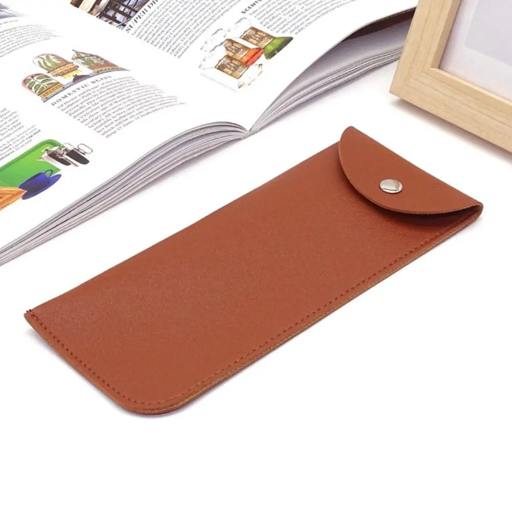 A brown PU leather eyewear case or glasses bag resting on a white surface next to an open magazine.