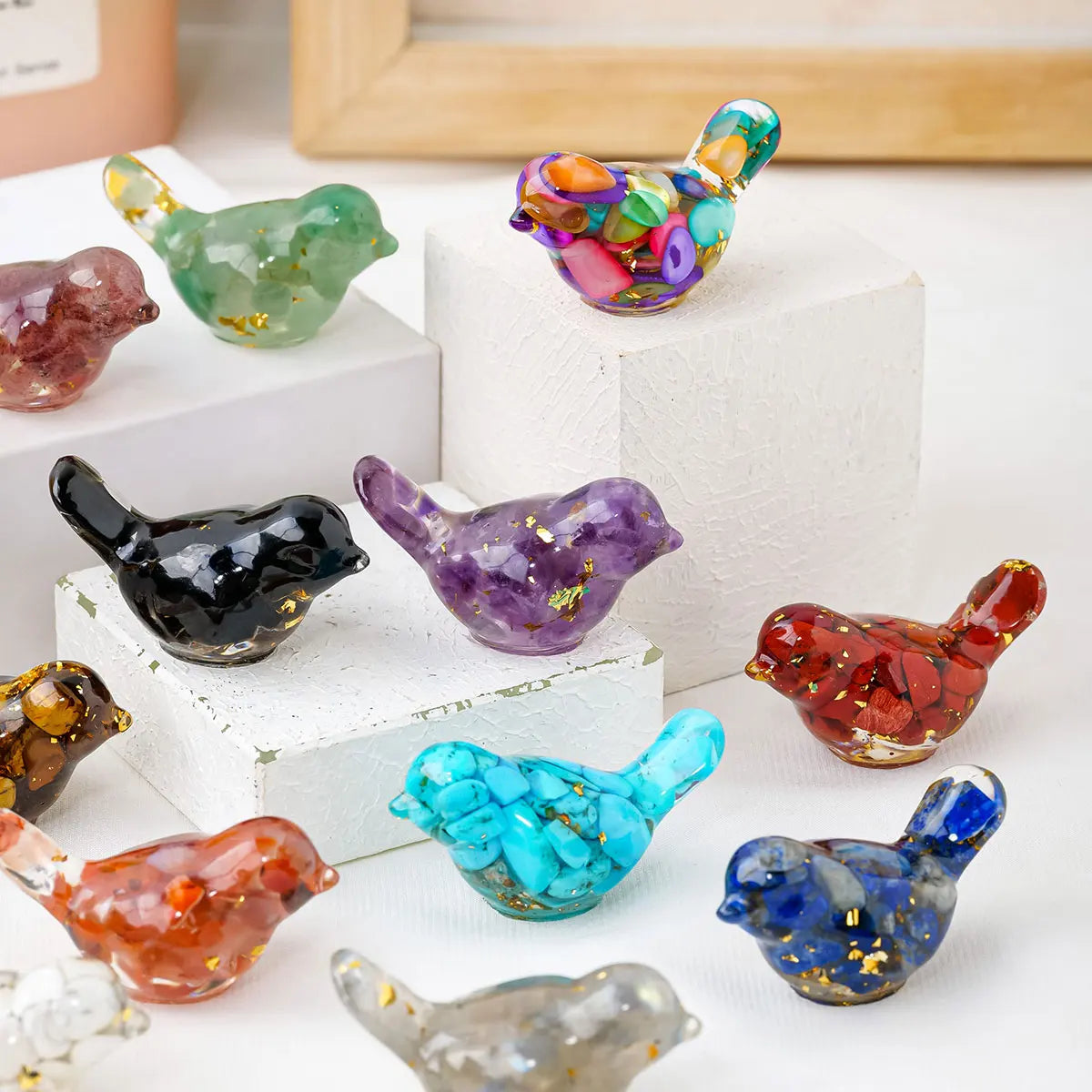 A collection of colorful crystal bird statues in various shades and sizes displayed on white blocks.