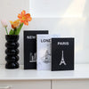 Three decorative fake books featuring city skylines, including New York, London, and Paris, displayed on a white shelf.