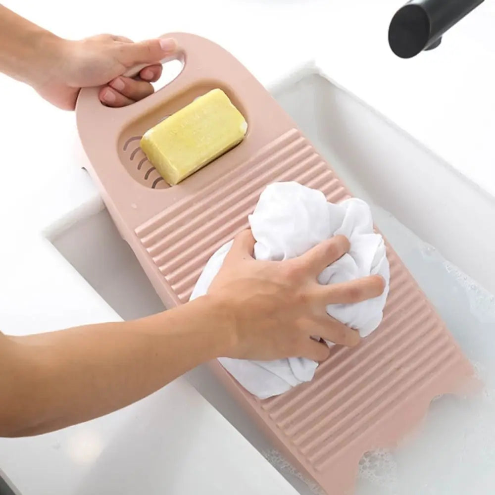 Hands place a yellow bar of soap and a white cloth onto a pink plastic washing board.