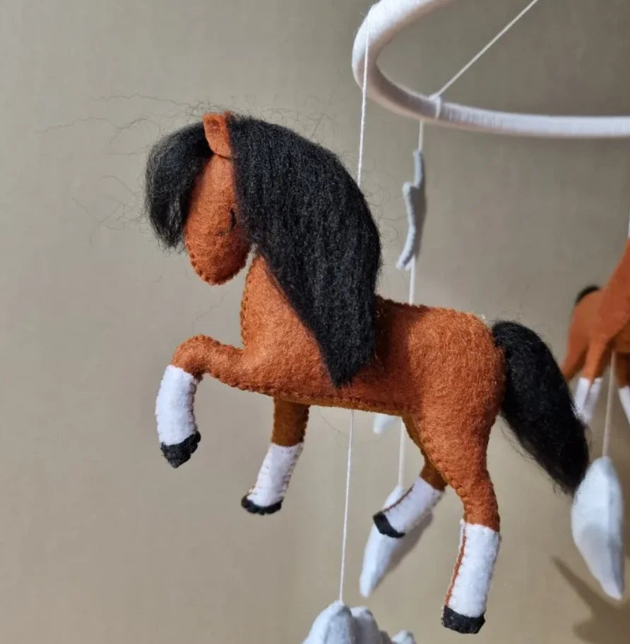 A brown and black felt horse hanging by its mane, displayed against a light background.