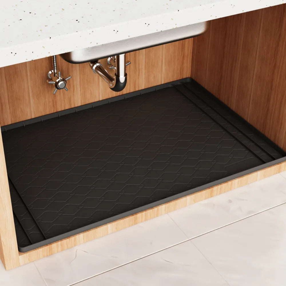 A dark silicone mat is placed inside a kitchen cabinet under the sink.