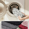 A hand is gently washing a gray pebble embossed bathroom rug inside a white washing machine drum.