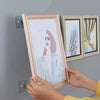 Hands holding a framed picture next to transparent self-adhesive wall hooks for frames and photos