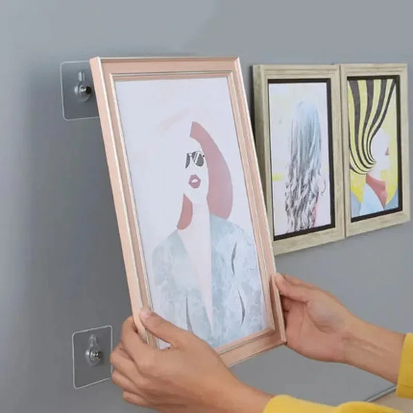 Hands holding a framed picture next to transparent self-adhesive wall hooks for frames and photos