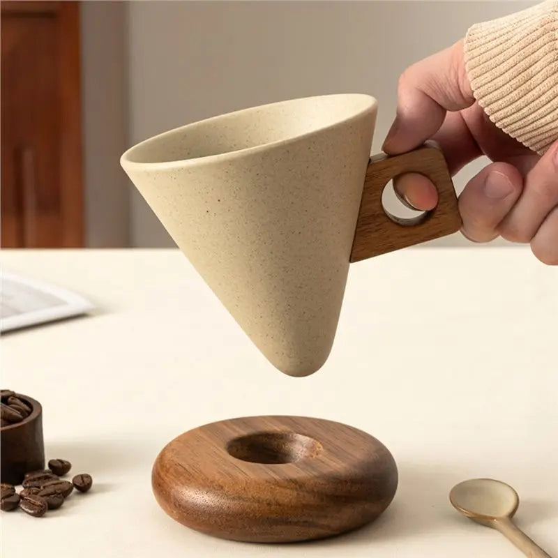 A hand holds a retro ceramic coffee mug with a wooden base and spoon set on a white surface.