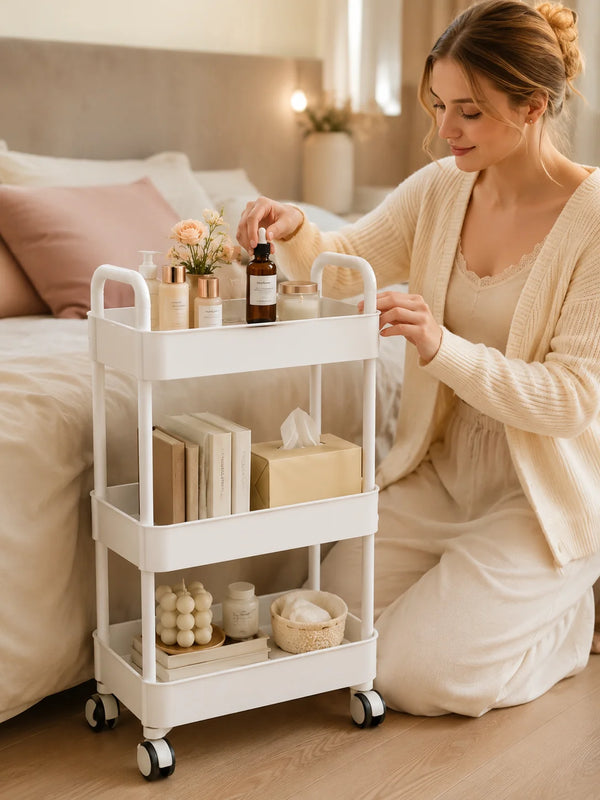 A woman is using a white 3-tier rolling storage cart with wheels to organize skincare products in a bedroom setting.
