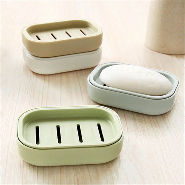 Three light green and beige compact travel soap cases with drainage slots resting on a wooden surface.