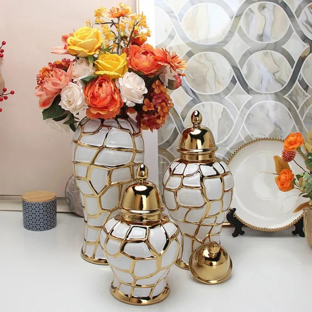 A collection of golden and white geometric ceramic flower vases displayed against a marbled background with an orange floral 