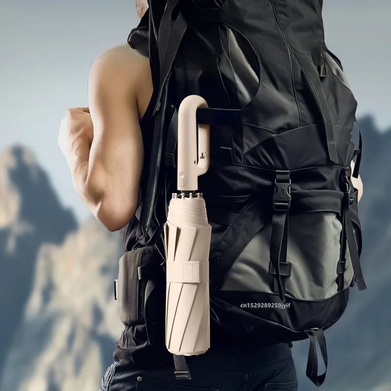 A beige automatic folding umbrella is shown attached to a black tactical vest, set against a mountainous outdoor background.