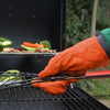 Orange quilted heat resistant oven mitts holding vegetables on a grill grate.