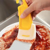 A hand is using a yellow silicone kitchen scraper to serve jam or preserves on a white plate.