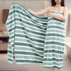 A woman holds a teal and white striped microfiber bath towel draped over her shoulder.