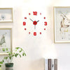 A round red and black analog wall clock with Roman numerals hangs on a white wall next to framed artwork.