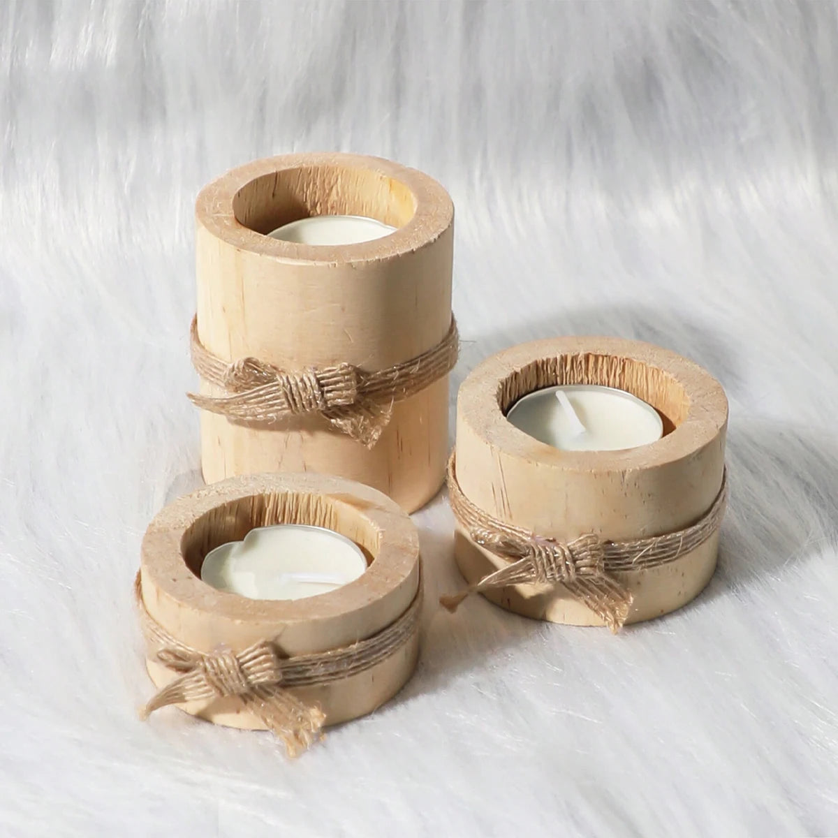 Tres portavelas de té de madera natural atados con cuerda sobre una superficie blanca y esponjosa.