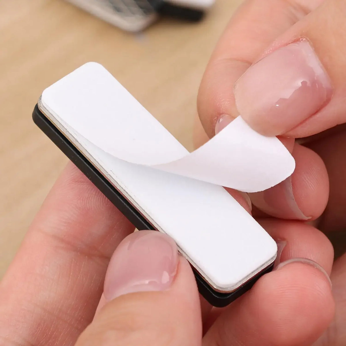 A hand holds a white magnetic curtain clip with a black backing and a white plastic wing, demonstrating its design.