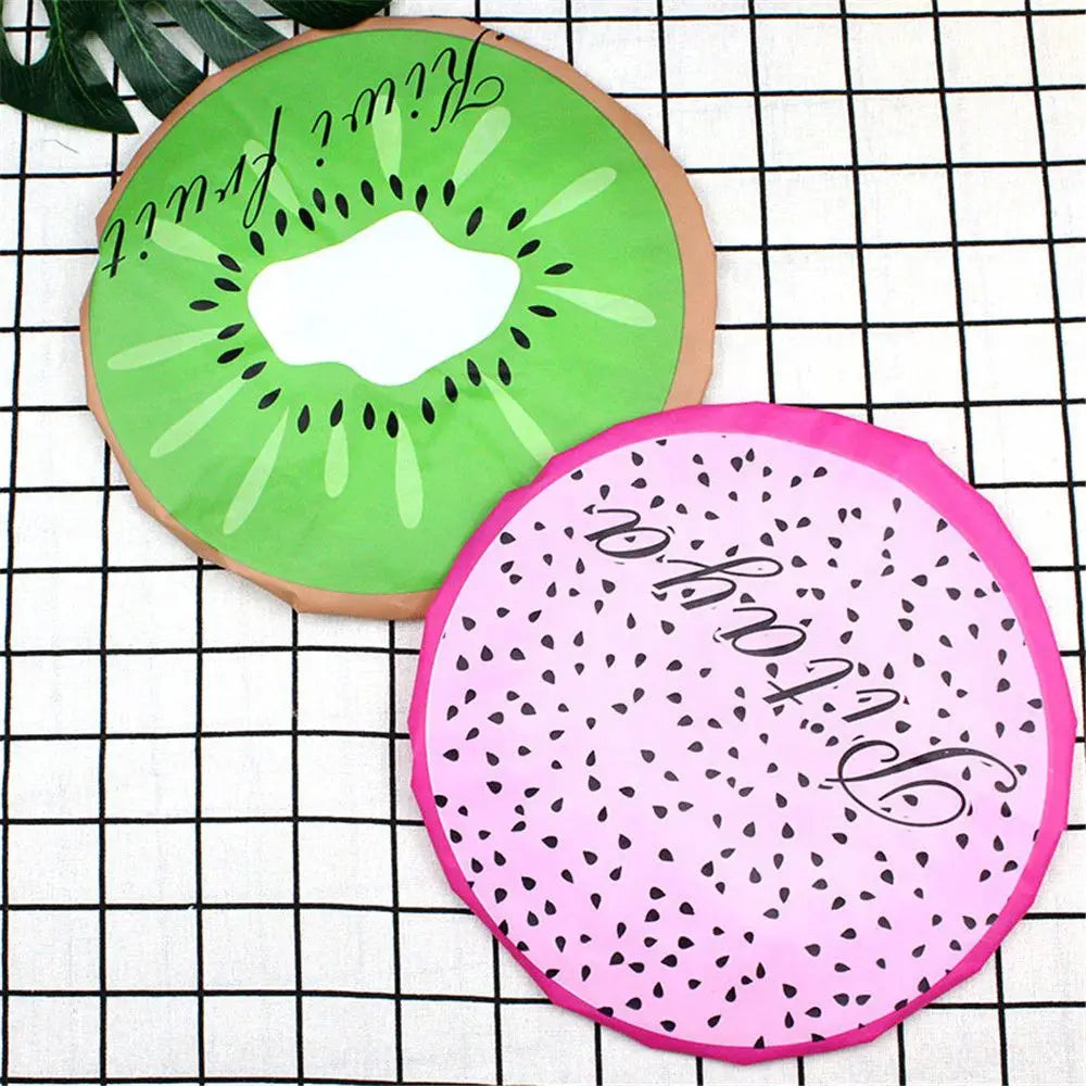 A reusable fruit shower cap shaped like a kiwi slice, pink, and green, placed on a black and white grid.