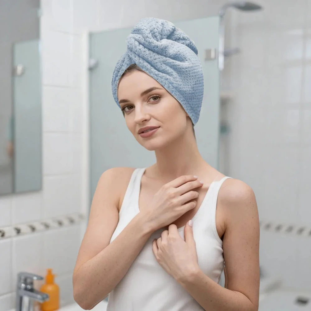 A woman wearing a light blue microfiber hair drying towel wrap in a bathroom setting.