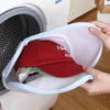 A hand is placing a red baseball cap into a white mesh reusable laundry bag.